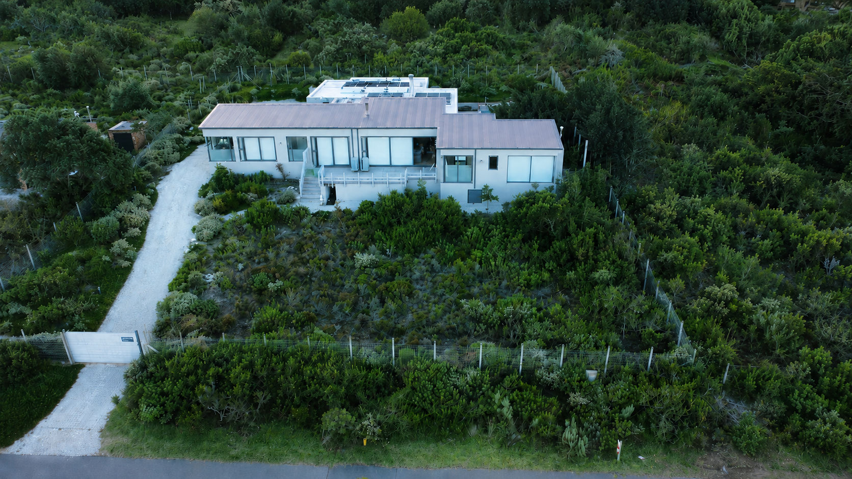 Aerial view of the Bass Road House, a modern home with metal roofs and solar panels among rocky fynbos terrain